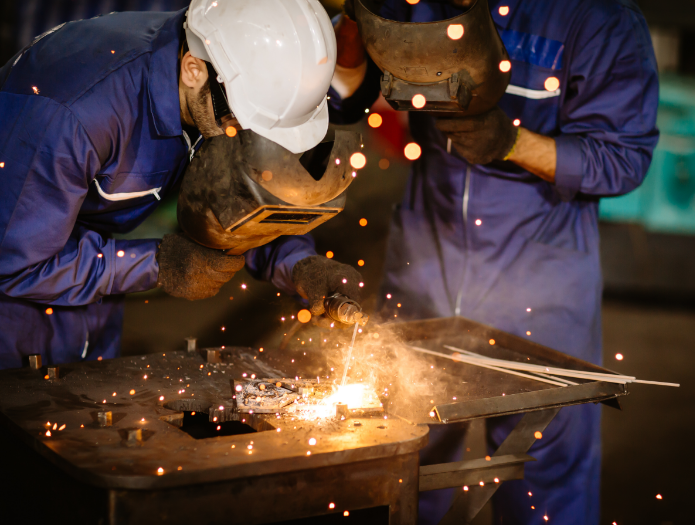 Two industrial workers welding metal with bright sparks.